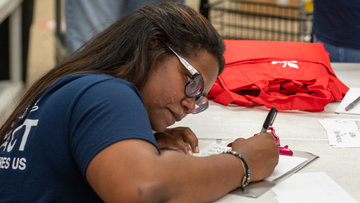 A woman holds a marker writing a letter on white paper. 