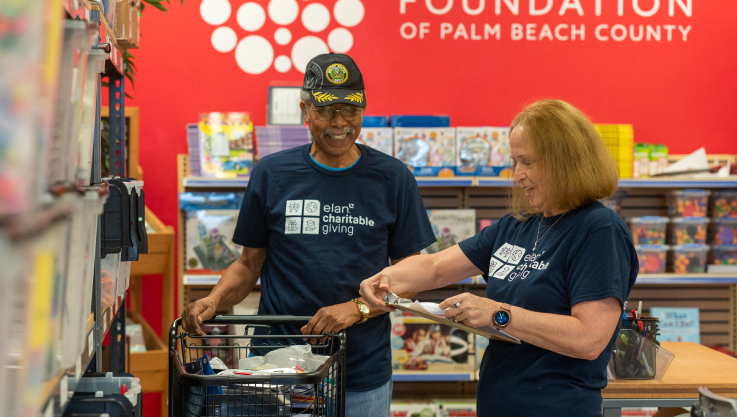 A man and woman wearing blue t-shirts stand with a clipboard and shopping cart. 