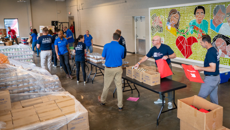 A group of individuals walk around a table of food filling bags as they move down the line. 