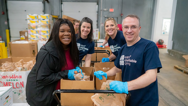 Four volunteers packing sweet potatoes smile at the camera.