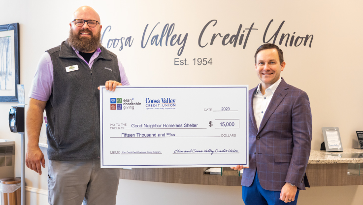 Two adults hold a large promotional check in a credit union lobby. 