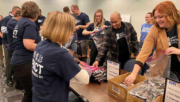 Adults walk down both sides of a long table picking up items as they go and putting in small bags.