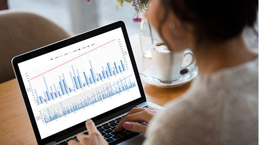 A female is typing on a laptop. The laptop screen is displaying graphs.